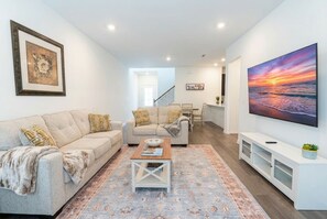 A modern living room with a sofa, coffee table, and a large TV on a white wall.