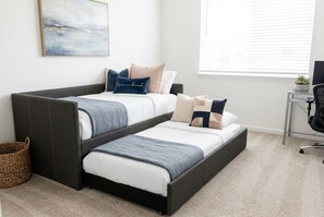 A bedroom with a bed, pillows, a bedside table, a chair, a window, and a wall-mounted painting. - Pool Jacuzzi | Gated community | 6 Min to Beach (Palm Coast)