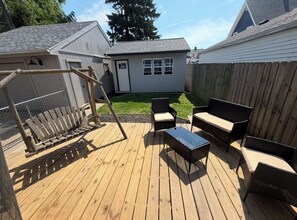 Una terraza de madera con mobiliario exterior, un columpio y un patio cercado.