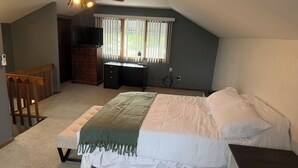 Une chambre à coucher comprenant un lit, un bureau, une chaise, un téléviseur et une fenêtre avec des stores.