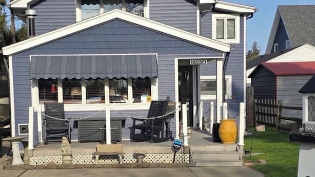 Une maison à deux étages avec un porche couvert, un garage dont la porte est visible et une cour clôturée.