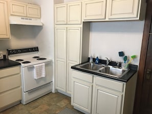 A compact kitchen with white cabinetry, a stove, and a sink.