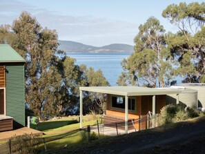 A coastal property with a wooden deck, a covered outdoor area, and a view of the sea and hills. - Breathtaking Views - 3 Bedroom House (Gordon)