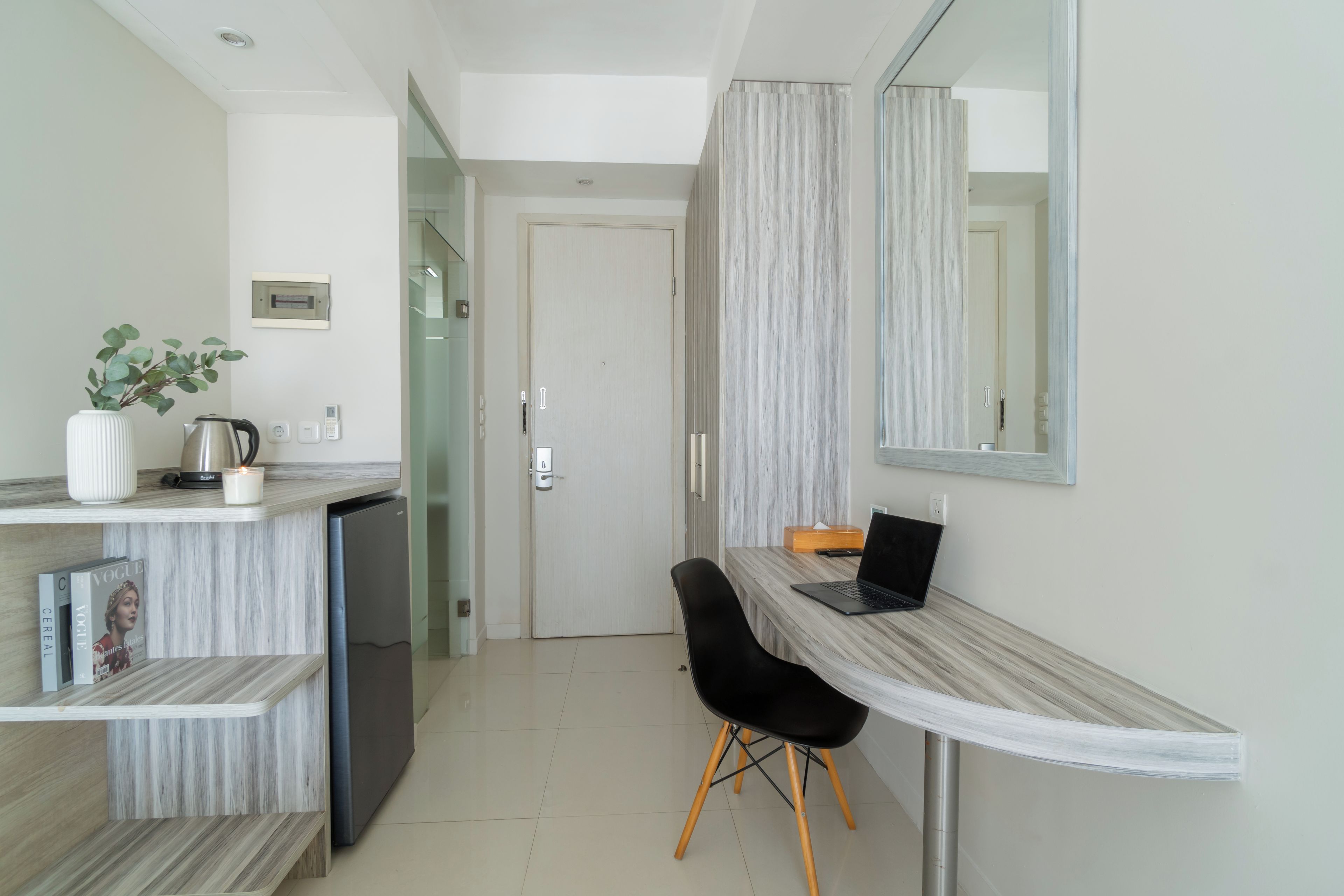 A modern hotel room with a kitchenette, a dining area with a laptop, and a large mirror.