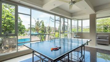 A ping pong table in a room with large windows, a ceiling fan, and a sofa.