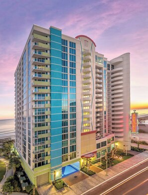 A multi-story hotel with a curved facade, a pool area, and a view of the beach.