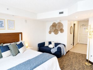 A hotel room with a bed, a seating area, a wall-mounted decorative piece, and a door leading to another room.