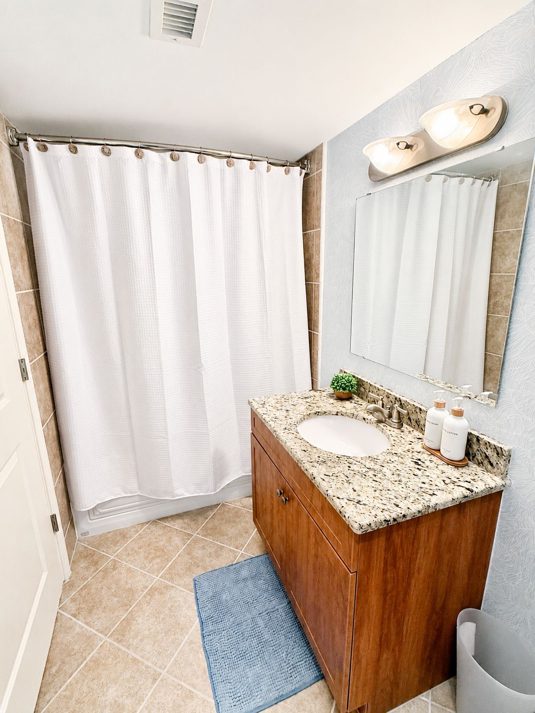 Un baño con cortina de ducha, un lavabo con encimera de mármol, un mueble de tocador de madera y un espejo.