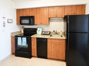 A kitchen with wooden cabinets, a black microwave, a black refrigerator, a coffee maker, and a dishwasher.