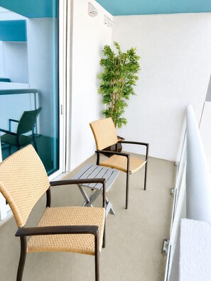 A balcony with wicker chairs and a small table, a potted plant, and a view of the interior.