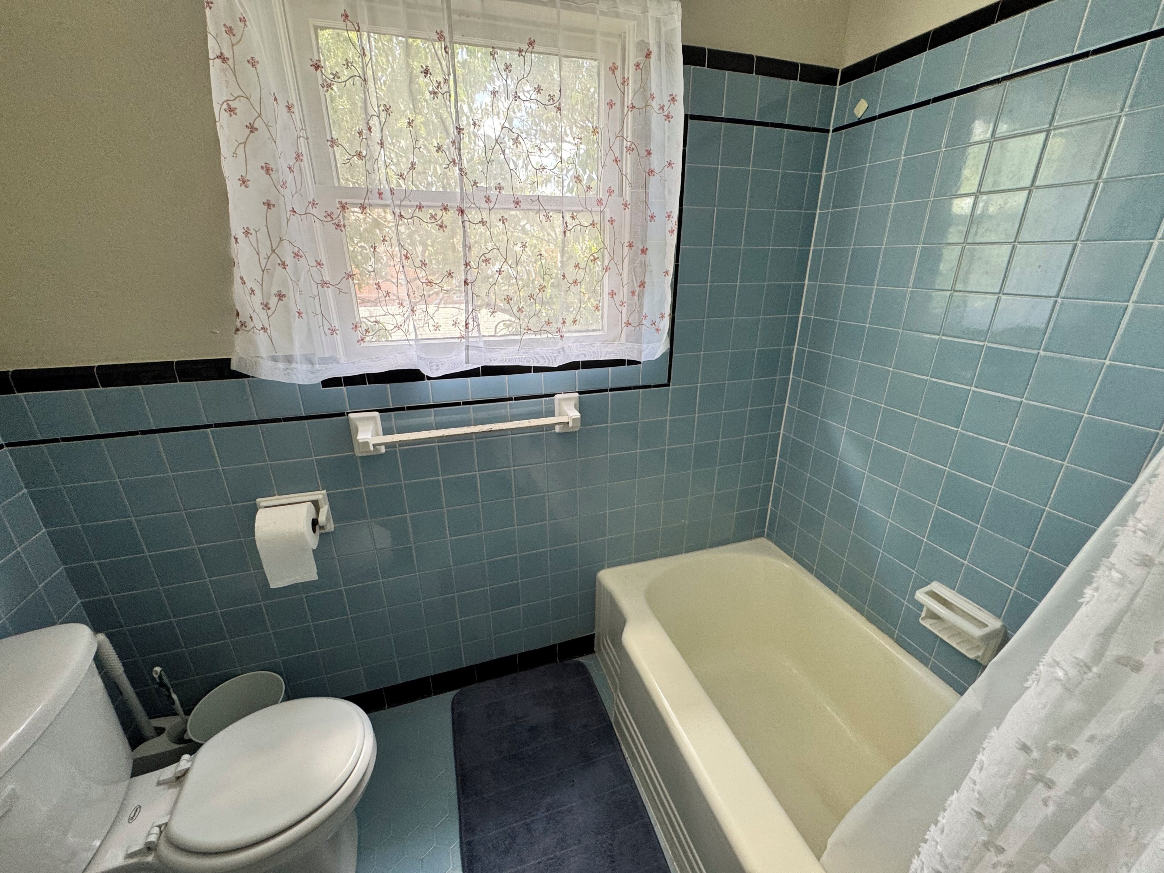 Een badkamer met toilet, badkuip en een raam met bloemen gordijnen.