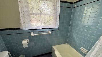 Ein Badezimmer mit Toilette, Badewanne und einem Fenster mit blumigem Vorhang.