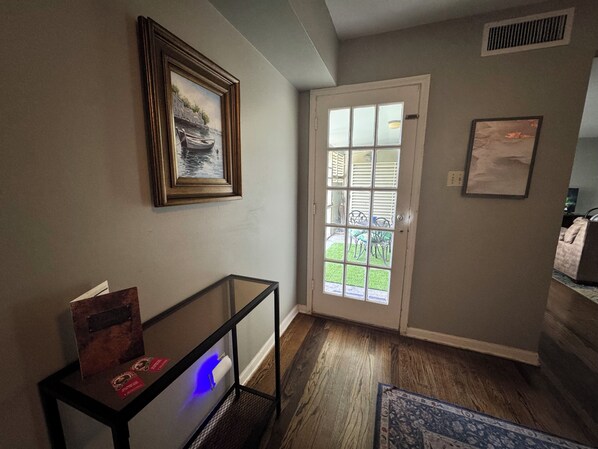 A hallway with a door leading to an outdoor area, a framed picture on the wall, and a small table with a lamp.