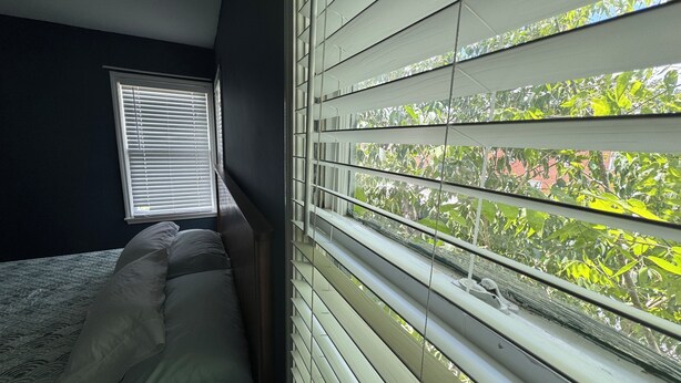 Una camera da letto con un letto, una finestra con persiane e vista sul verde.