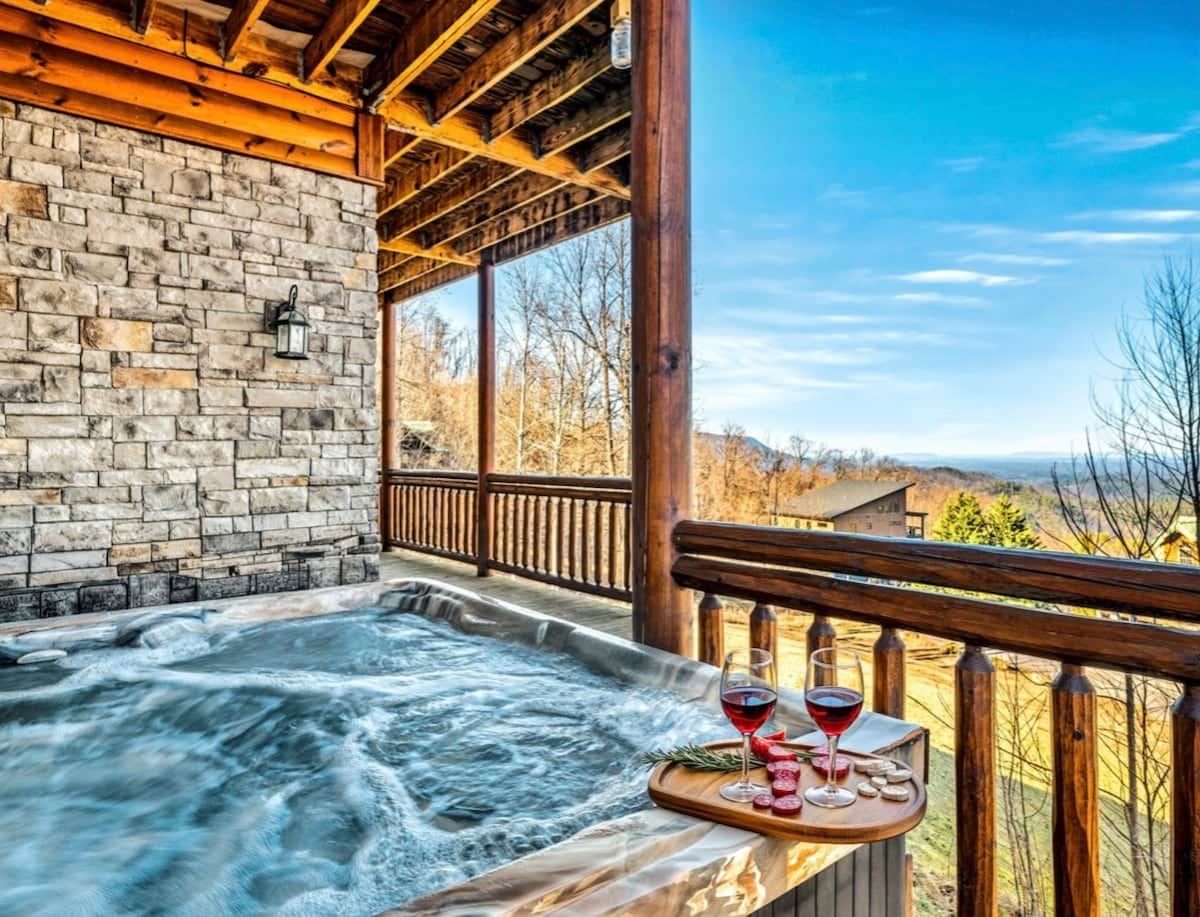 Een hottub met een houten terras, een stenen muur en een prachtig uitzicht.