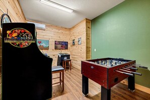 Quarto com mesa de pebolim, área de bar com banquetas e televisão na parede.