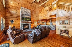 A log cabin interior with a stone fireplace, leather sofas, and a kitchen area. - Blue Hue Horizon Lodge spacious 4-bedrooms/4 bath (9 beds) (Sevierville)