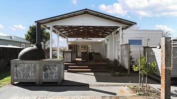 A covered patio area with a barbecue grill, steps leading to a house, and a small garden with plants.