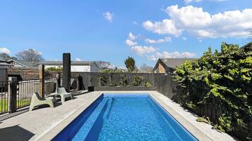 A rectangular swimming pool with clear blue water, surrounded by a concrete deck and a wooden fence.