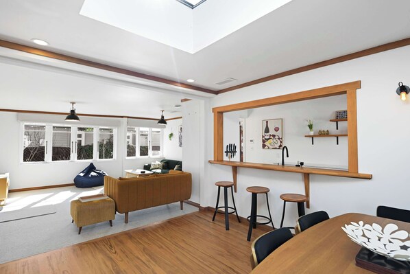 A modern living room with a wooden floor, a sofa, a dining table with chairs, and a large window with multiple panes.