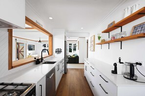 A modern kitchen with white cabinetry, a central island, and a view into the living area. - A True Victorian | Spa, Pool & Sauna (Cambridge)