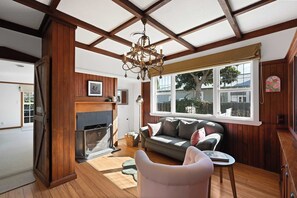 A cozy living room with a fireplace, a sofa, a chair, and a large window with a view of the outside.