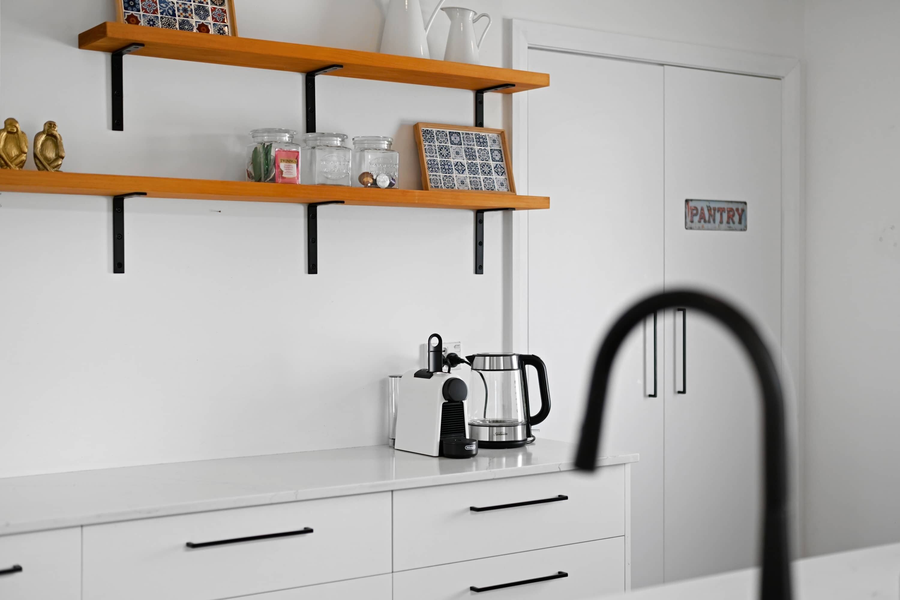 A kitchen with white cabinets, a coffee maker, and a pantry sign.
