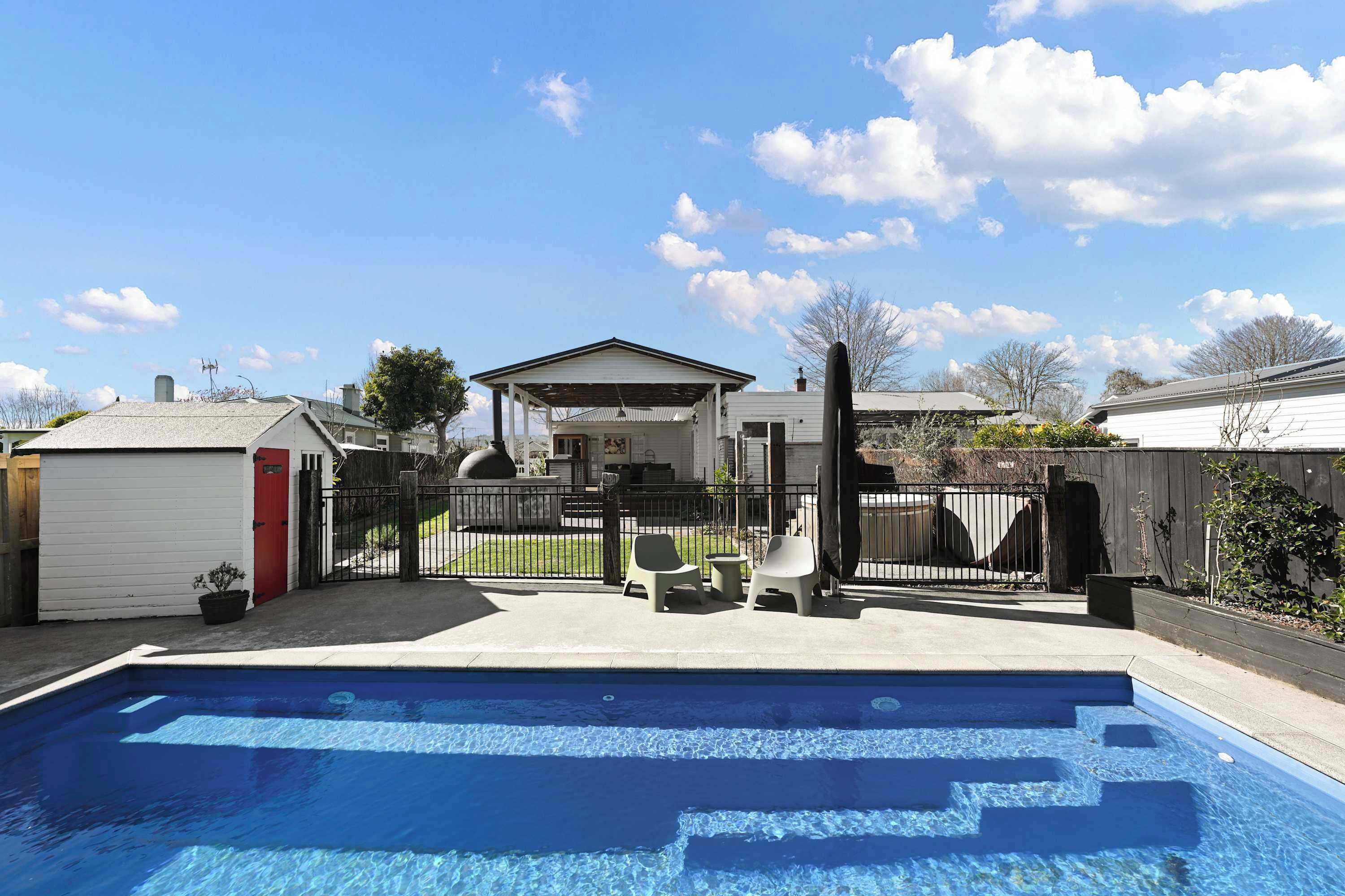 A backyard with a swimming pool, a covered patio area, and a fenced yard.