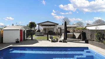 A backyard with a swimming pool, a covered patio area, and a fenced yard.