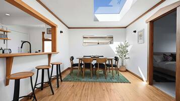 Ein kompakter Raum mit Dachfenster, einer Essecke mit Tisch und Stühlen sowie einer Bar mit Hockern.