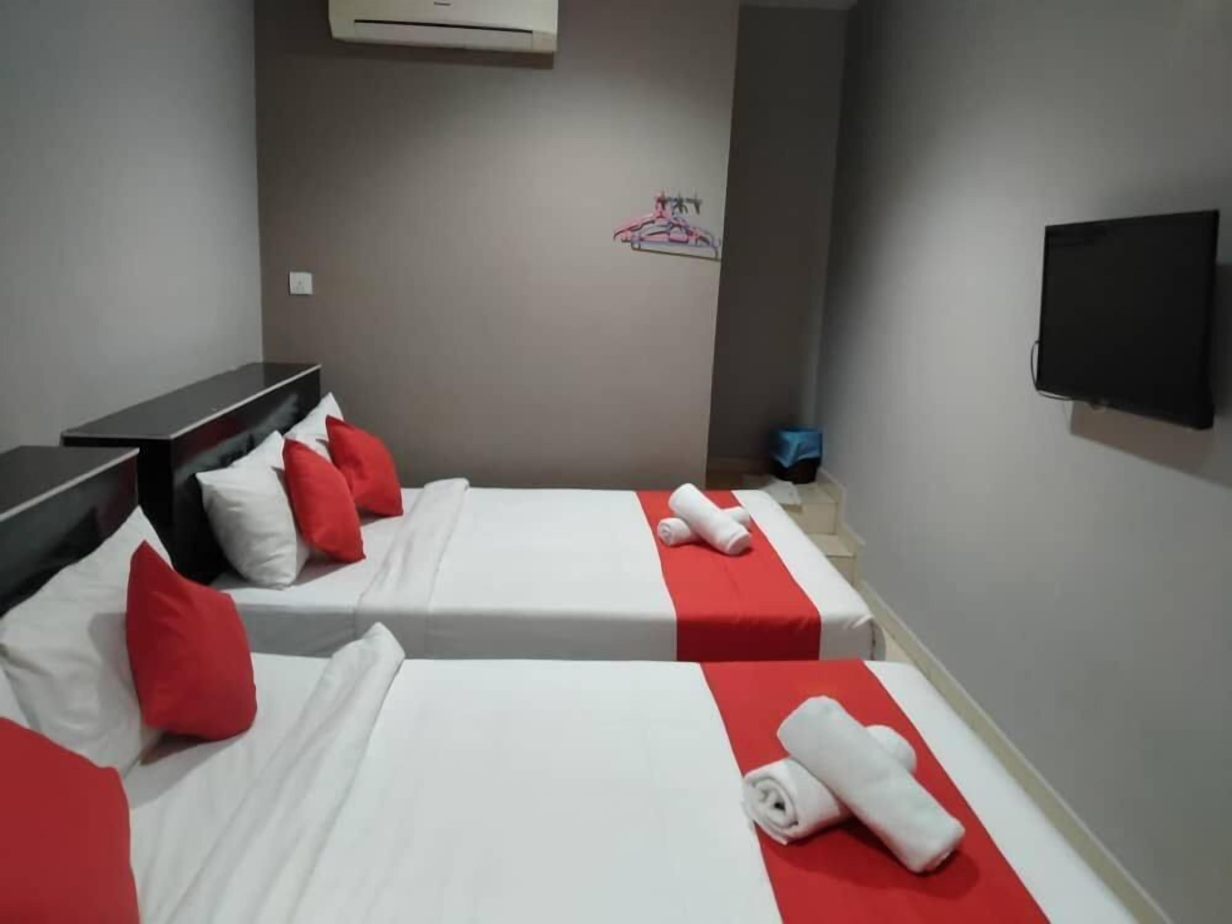 Ein Hotelzimmer mit zwei Betten, jeweils mit roter und weißer Bettwäsche, einem an der Wand befestigten Flachbildfernseher und einem kleinen Tisch.