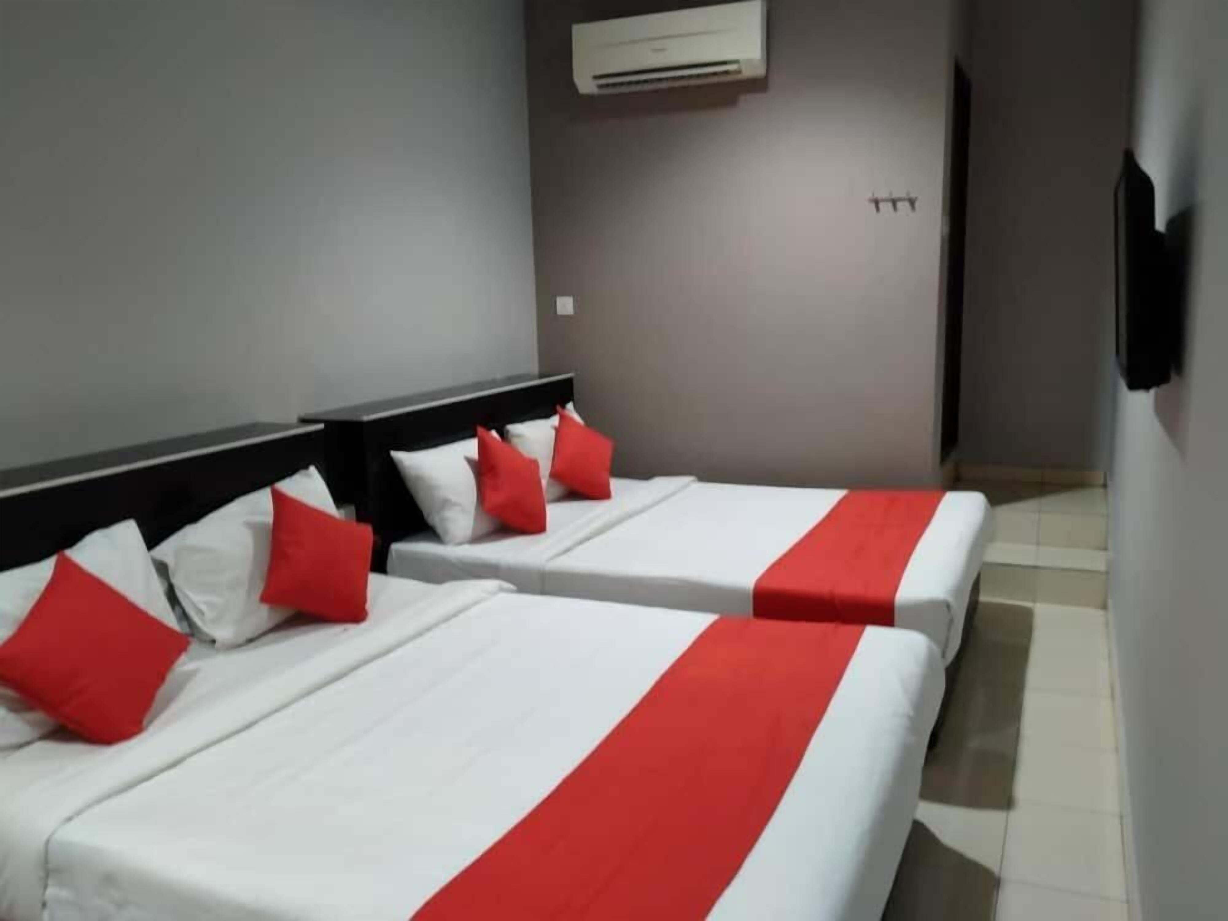 A hotel room with two beds, each with white bedding and red accents, a wall-mounted air conditioner, and a tiled floor.