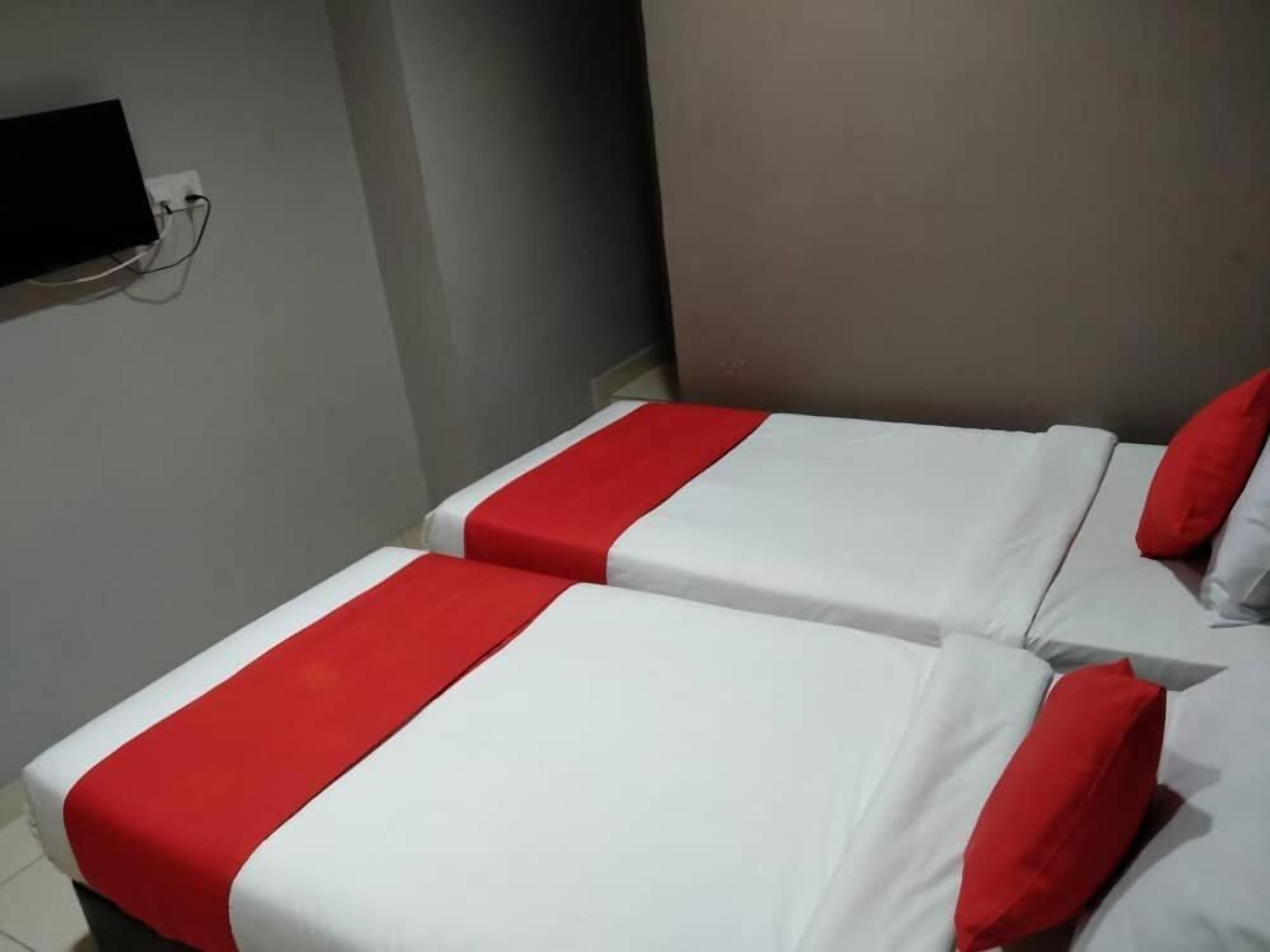 Two beds with red and white bedding, a wall-mounted television, and a grey wall.