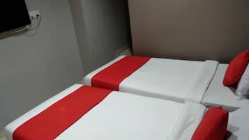 Two beds with red and white bedding, a wall-mounted television, and a grey wall.