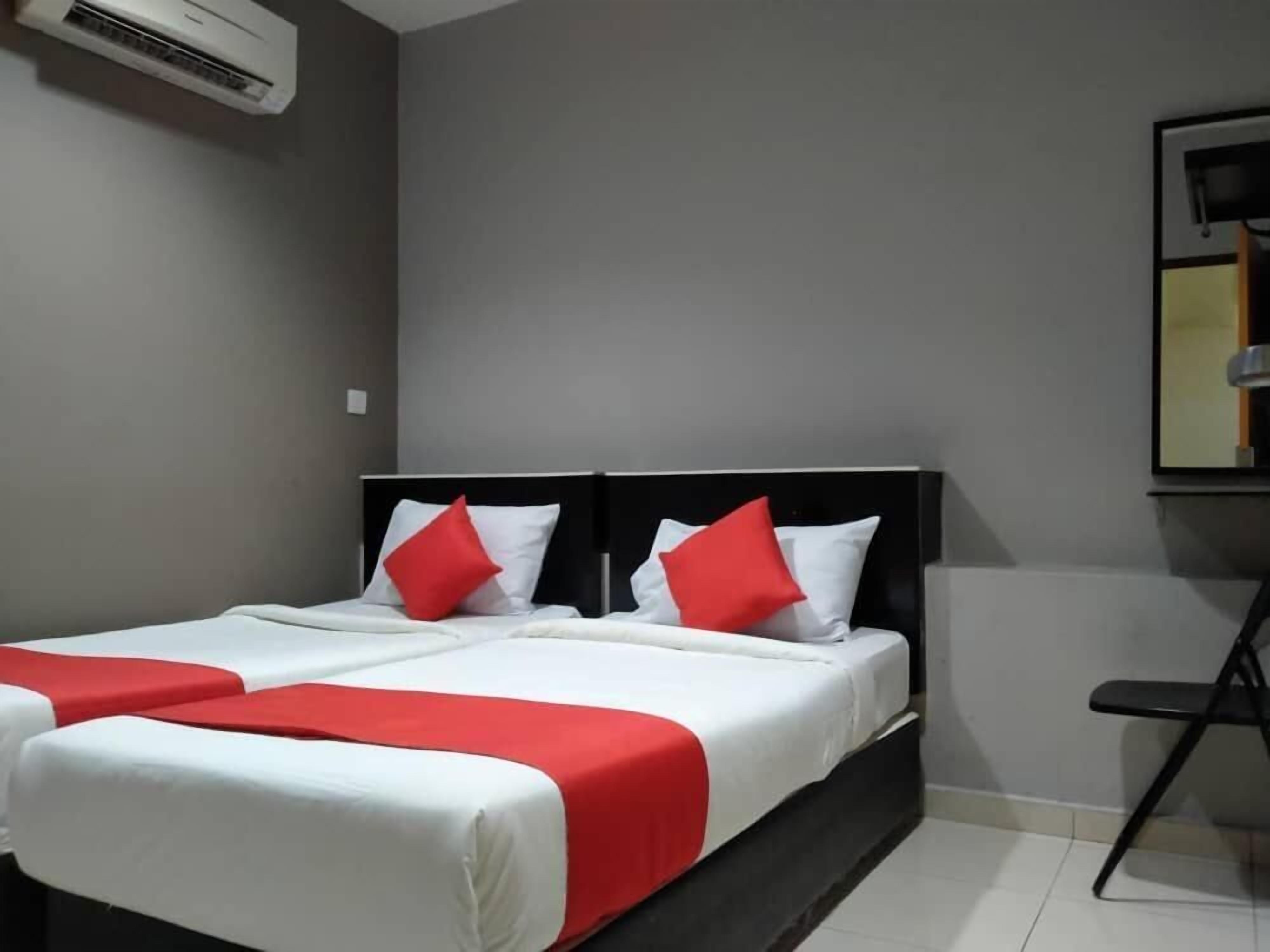A hotel room with two beds, each with white bedding and red accents, a black headboard, and a wall-mounted air conditioner.