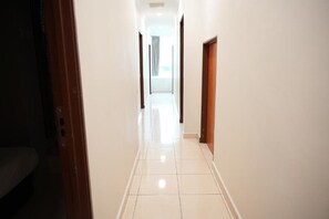 A corridor with a tiled floor leading to a bright room with a door at the end.