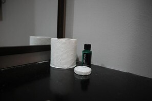 Una encimera de baño con un rollo de pañuelos, un dispensador de gel antibacterial y una barra de jabón.