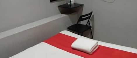 A hotel room with a bed, a TV mounted on the wall, a small table, and a chair.