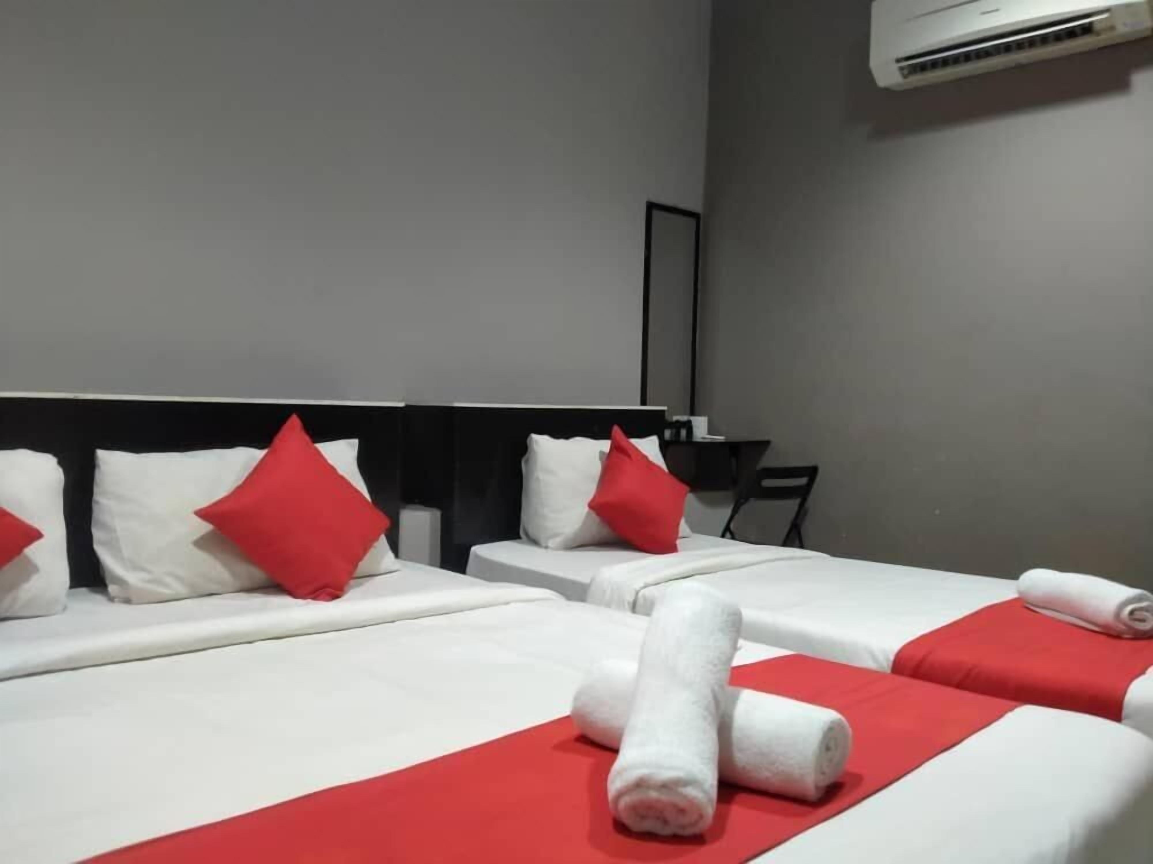 Habitación de hotel con dos camas, cada una con ropa de cama blanca y detalles en rojo, y una toalla roja sobre la cama.