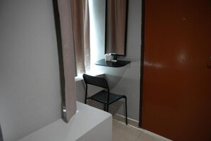Una habitación pequeña con una silla, una mesa, un ventanal con cortinas y una puerta.