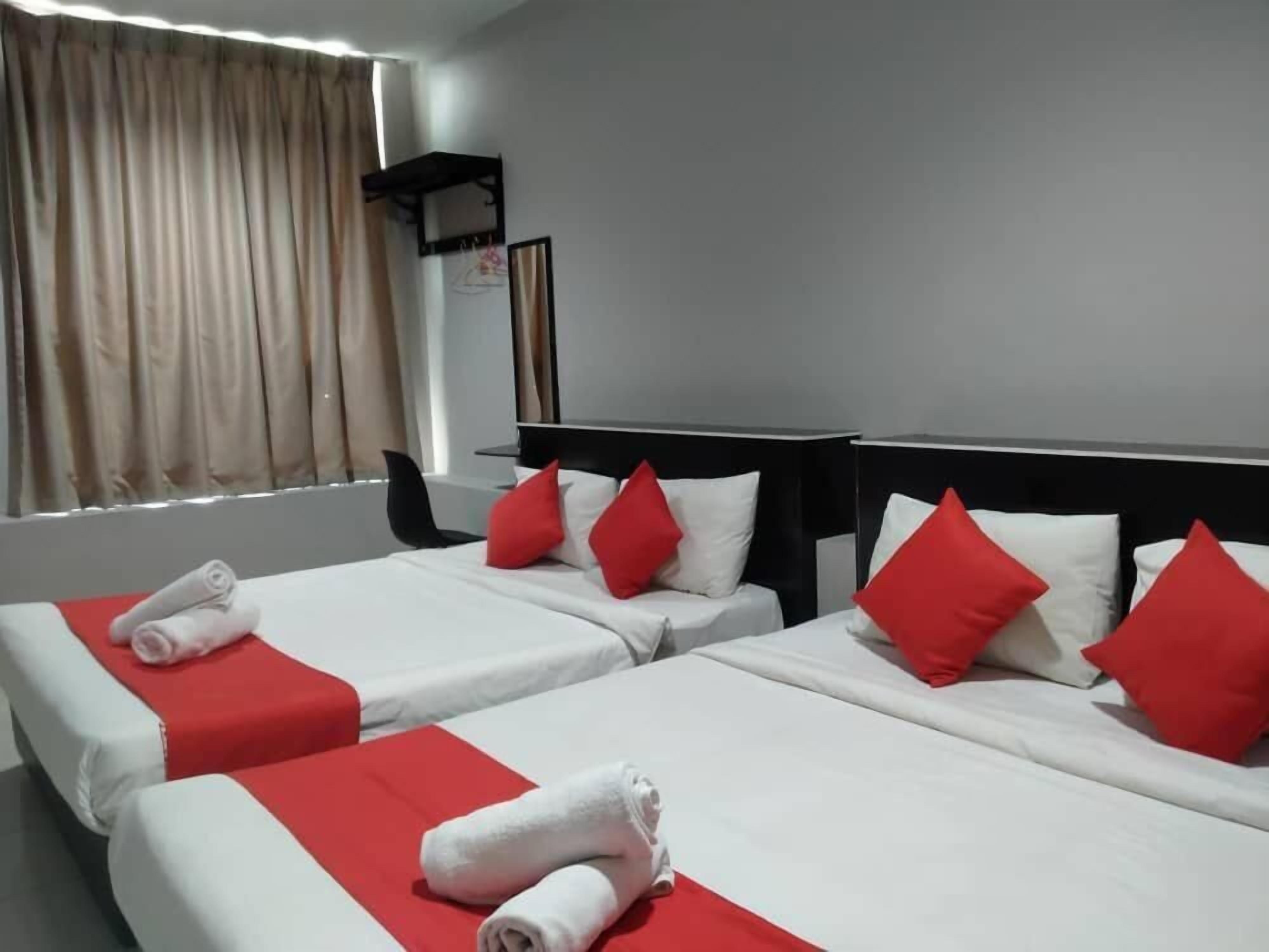 Une chambre d’hôtel avec deux lits, chacun agrémenté de draps rouges et blancs, et une fenêtre avec des rideaux.