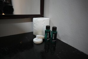 Una encimera de baño con un rollo de papel higiénico blanco, dos botellas de acondicionador Divine y una barra de jabón.