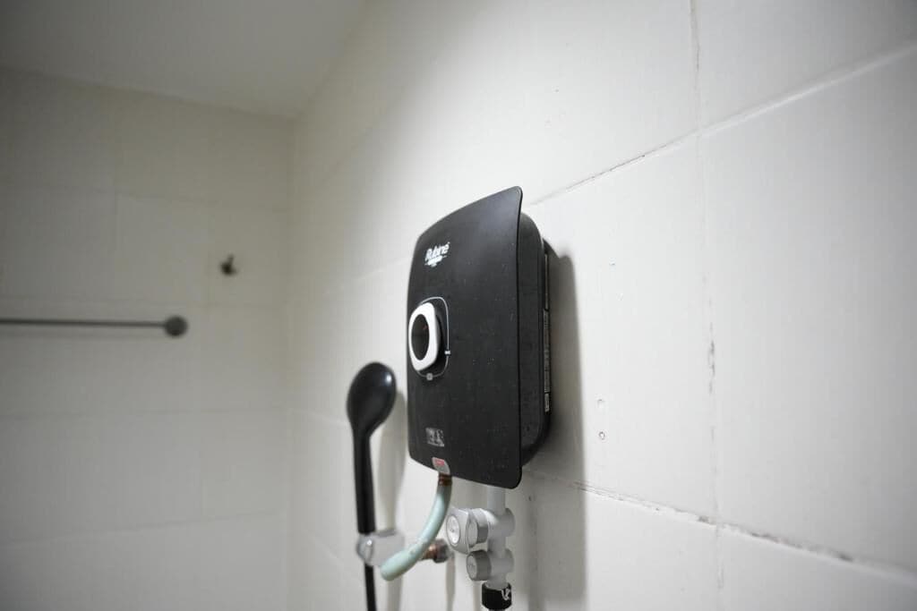 A bathroom with a black object mounted on the wall, a towel rack, and a pipe.