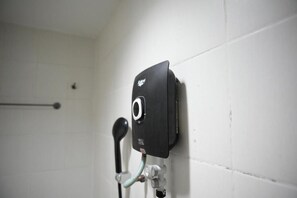 Un baño con un objeto negro sujeto a la pared, un perchero y una tubería.