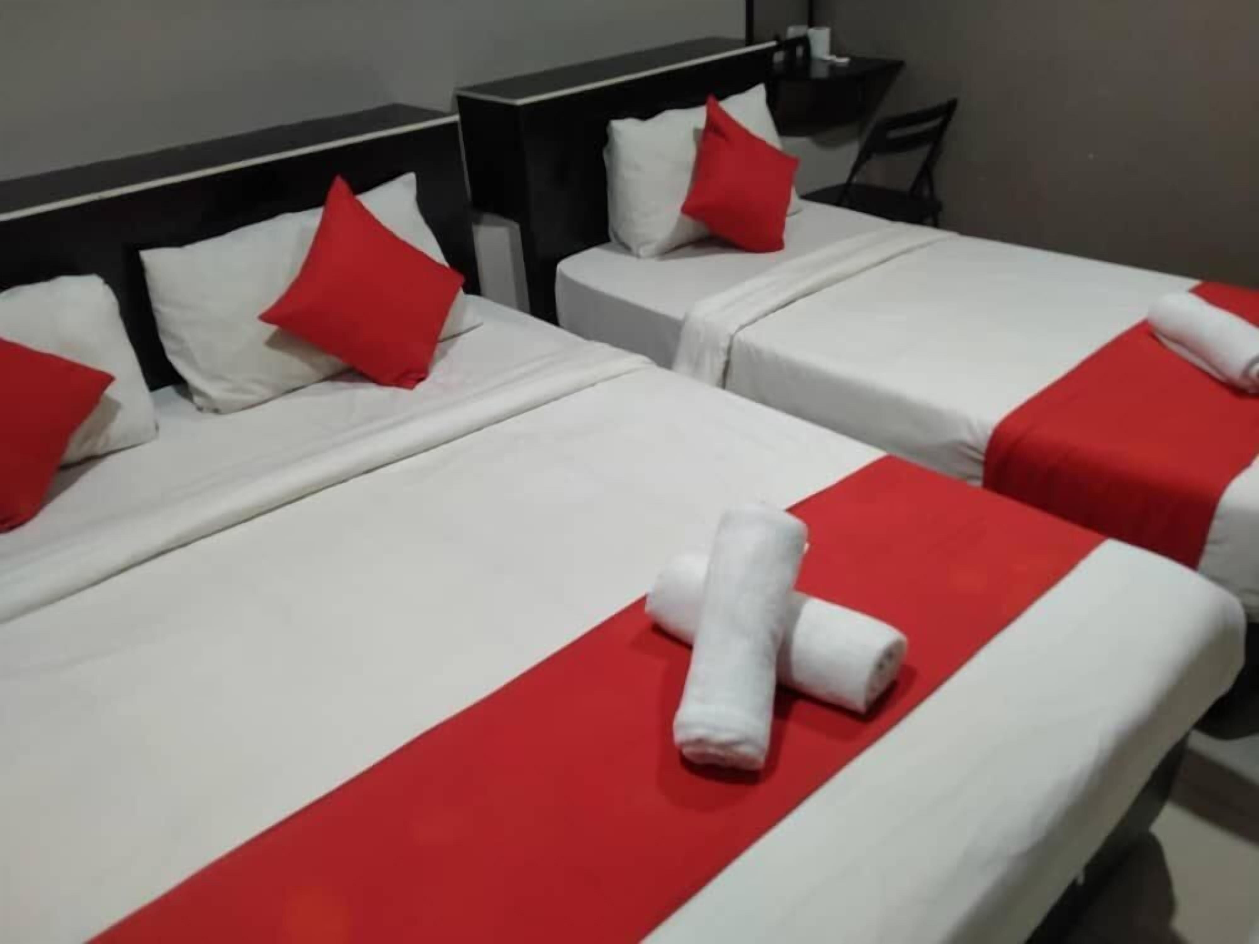 Two beds with white and red bedding, pillows, and rolled towels.