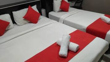 Two beds with white and red bedding, pillows, and rolled towels.