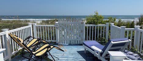 A wooden deck with two sun loungers and a gate, overlooking a beach.