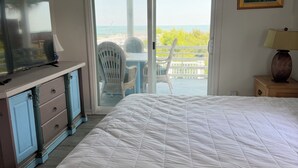 Un dormitorio con una cama grande, televisión, cómoda y vista al océano a través de una puerta corrediza.