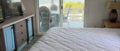 Un dormitorio con una cama grande, televisión, cómoda y vista al océano a través de una puerta corrediza.