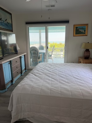 Un dormitorio con una cama grande, televisión, cómoda y vista al océano a través de una puerta corrediza.